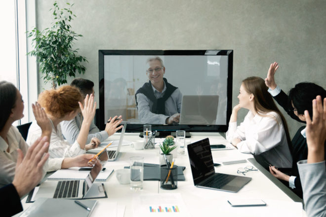 Mitarbeiter um einen Tisch und zugeschaltet in einer Videokonferenz erfordert ein geschicktes Telko einrichten