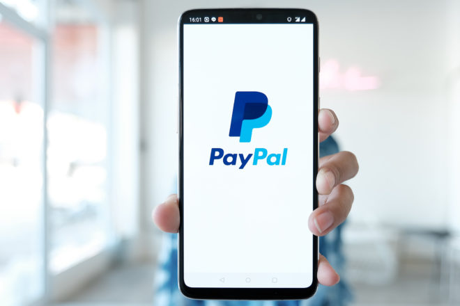 Foto zeigt eine Hand die ein Smartphone mit Paypal-Logo auf dem Bildschirm zeigt und über das Unternehmer und Verbraucher rasch per Paypal Kredit beanspruchen können.