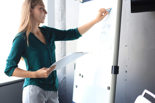 Foto zeigt junge Frau, die auf einem Whiteboard schreibt während einer Weiterbildung zur Nachwuchsförderung im Unternehmen