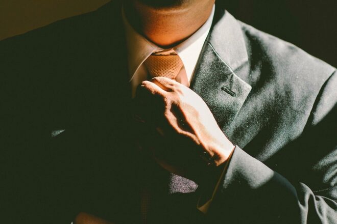 Foto zeigt Ausschnitt von Mann im Anzug, der sich die Krawatte richtet welche sich aber nicht als Arbeitskleidung von der Steuer absetzen lässt