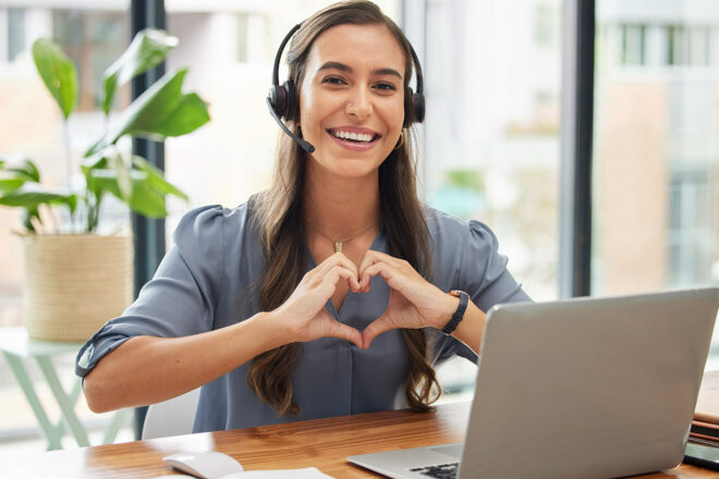Foto zeigt eine Frau am Laptop mit Kopfhörern mit den Händen in Herzform zum Thema Employer Branding