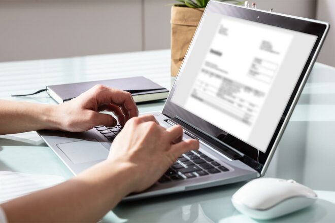 Foto zeigt Hände auf einer Laptoptastatur und auf dem Bildschirm eine Rechnung oder Kleinbetragsrechnung