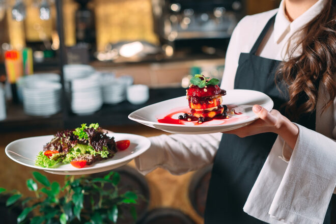 Foto zeigt Hände einer Kellnerin im Midijob mit Tellern Salat und Pastete