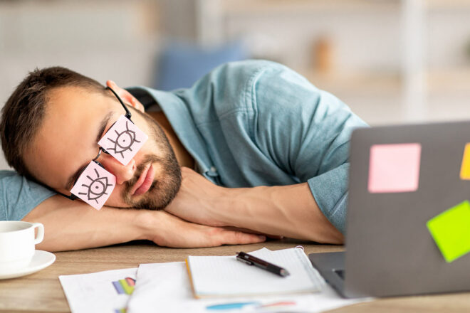 Das Bild von einem Mann, der mit dem Kopf auf dem Schreibtisch schläft, symbolisiert das Thema der Abmahnung und Kündigung an einen Minderleister wegen der Minderleistung.