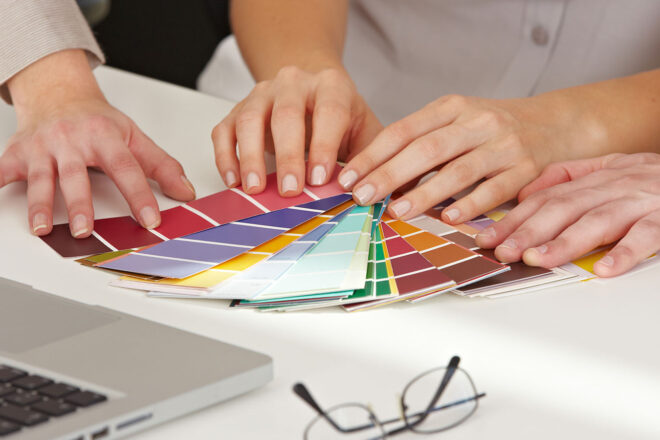 Mehrere Hände blättern durch Farbmuster für die Farbgestaltung im Büro