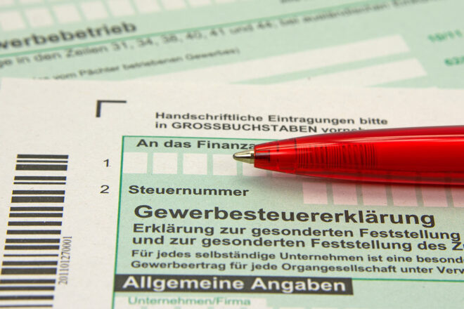 Foto zeigt roten Kugelschreiber auf Steueranlageformular für Gewerbesteuer - was sie ist und wer sie zahlt